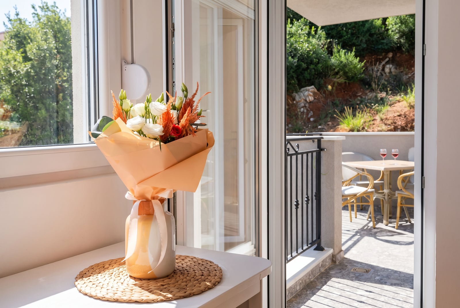 A bouquet of flowers on a living room table in a Budva apartment, Montenegro, with access to a cozy terrace featuring garden furniture.