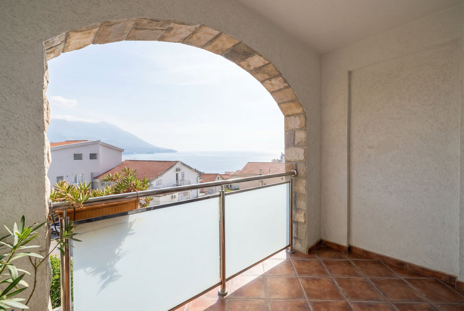 Balcony with a stone arch and sea view at a hotel in Bečići, Montenegro: tiled floor and glass railing.