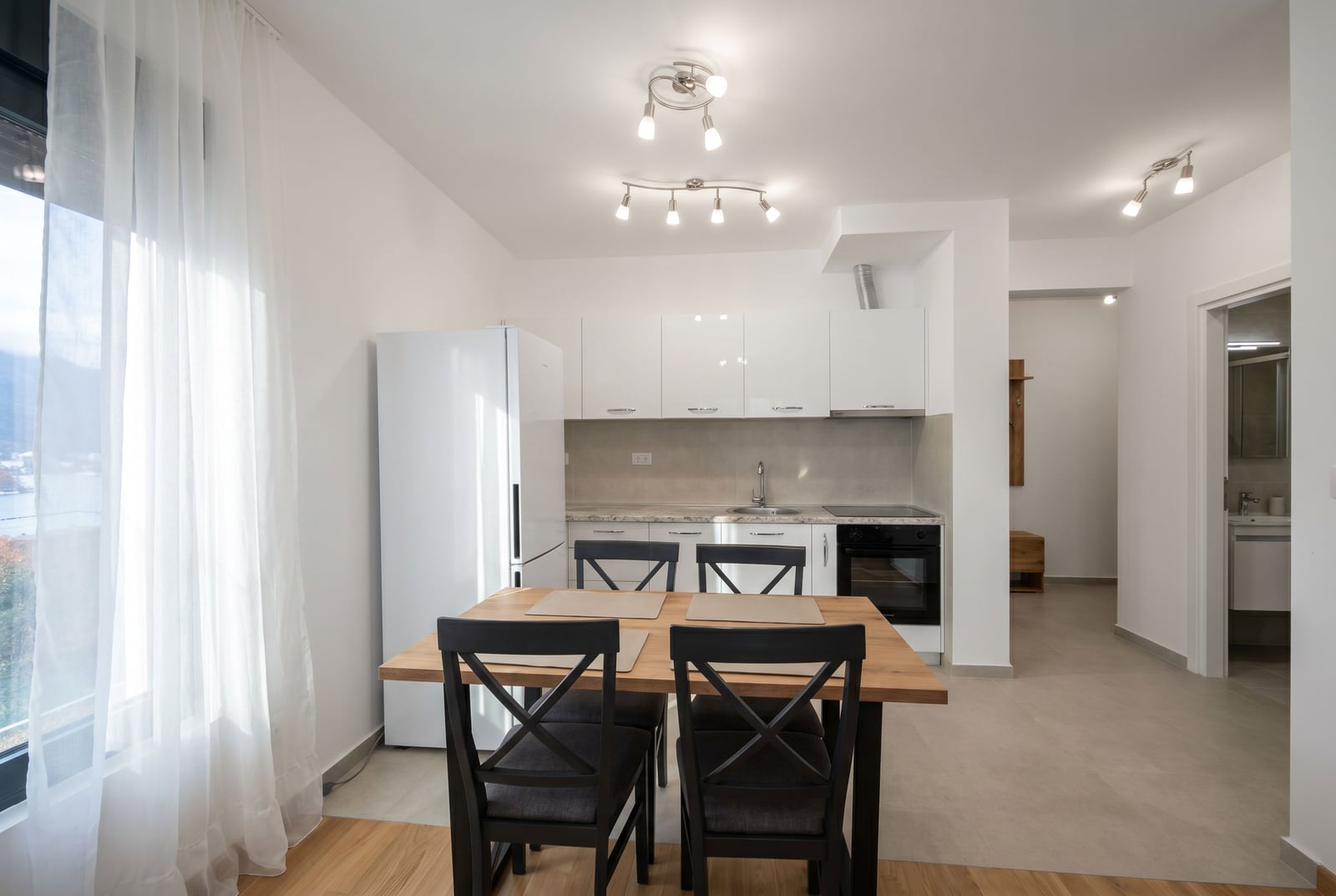 Modern kitchen-dining room in an apartment in Becici, Montenegro: white cabinetry, wooden table, and sea view.