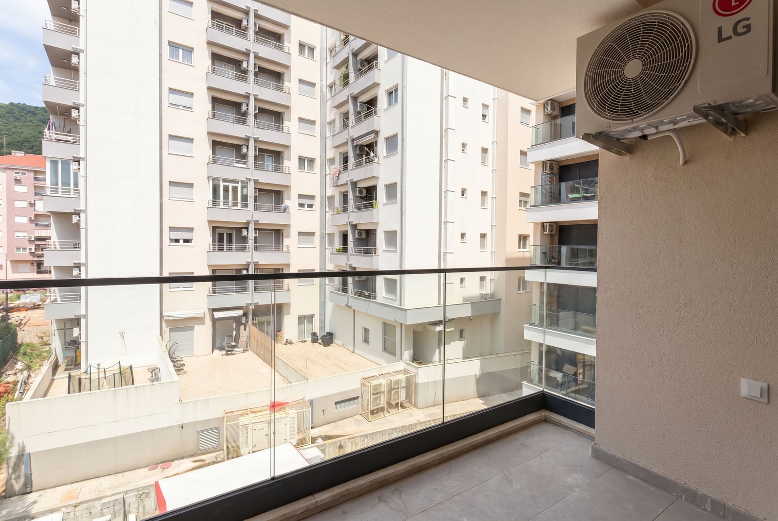 Balcony of a modern apartment in Budva, Montenegro, with panoramic glass railings and a view of the residential complex.