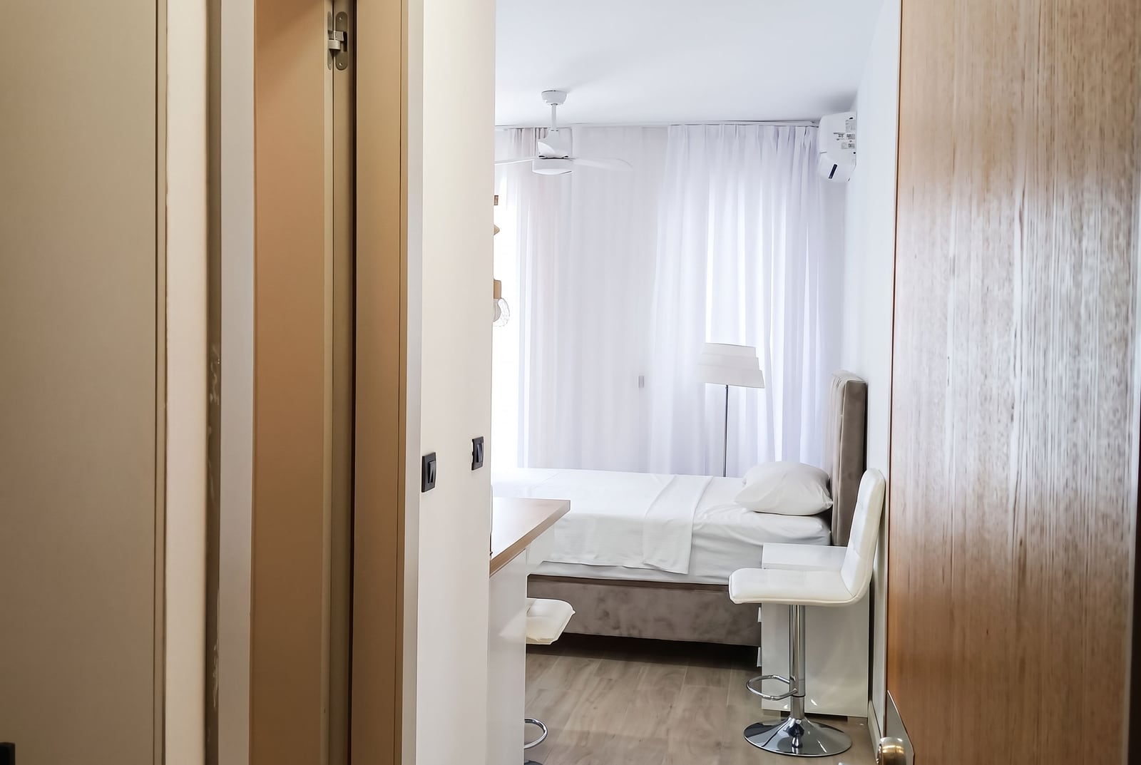 Bright bedroom in an apartment in Bečići, Montenegro: double bed, white curtains, air conditioning, and bar stools.