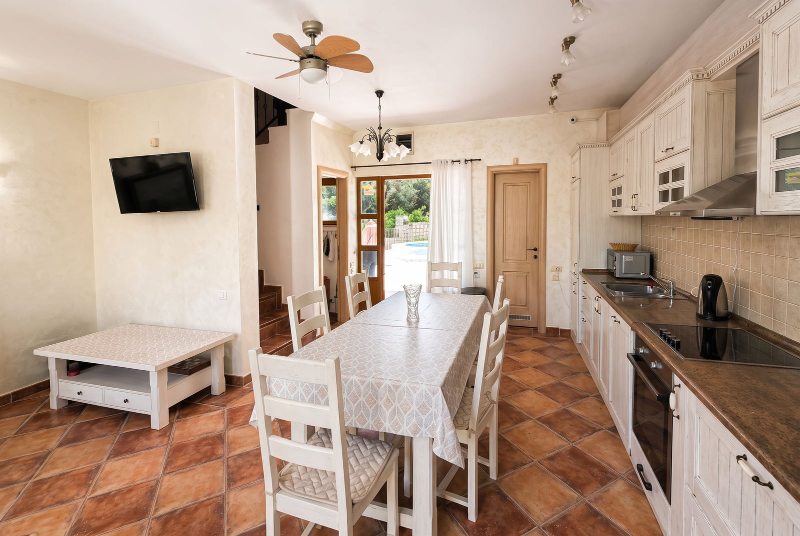 Kitchen with dining area, white cabinets, stove, and wall-mounted TV.