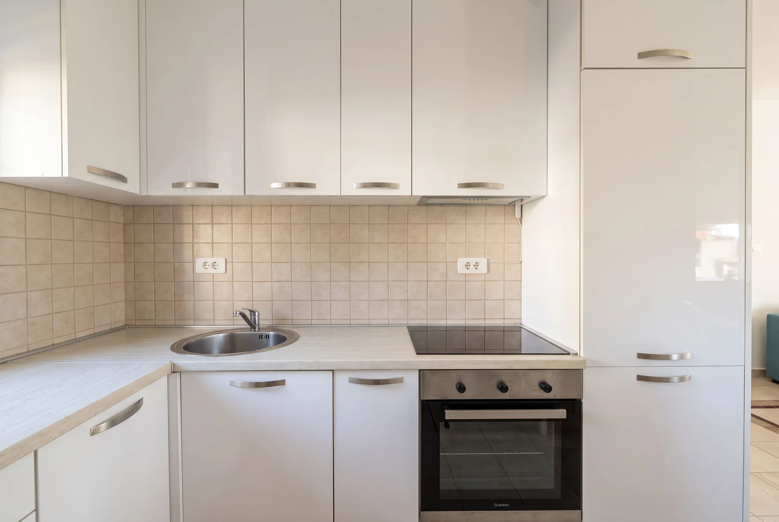 Modern kitchen with white cabinets, a sink, induction cooktop, and oven on a light countertop.