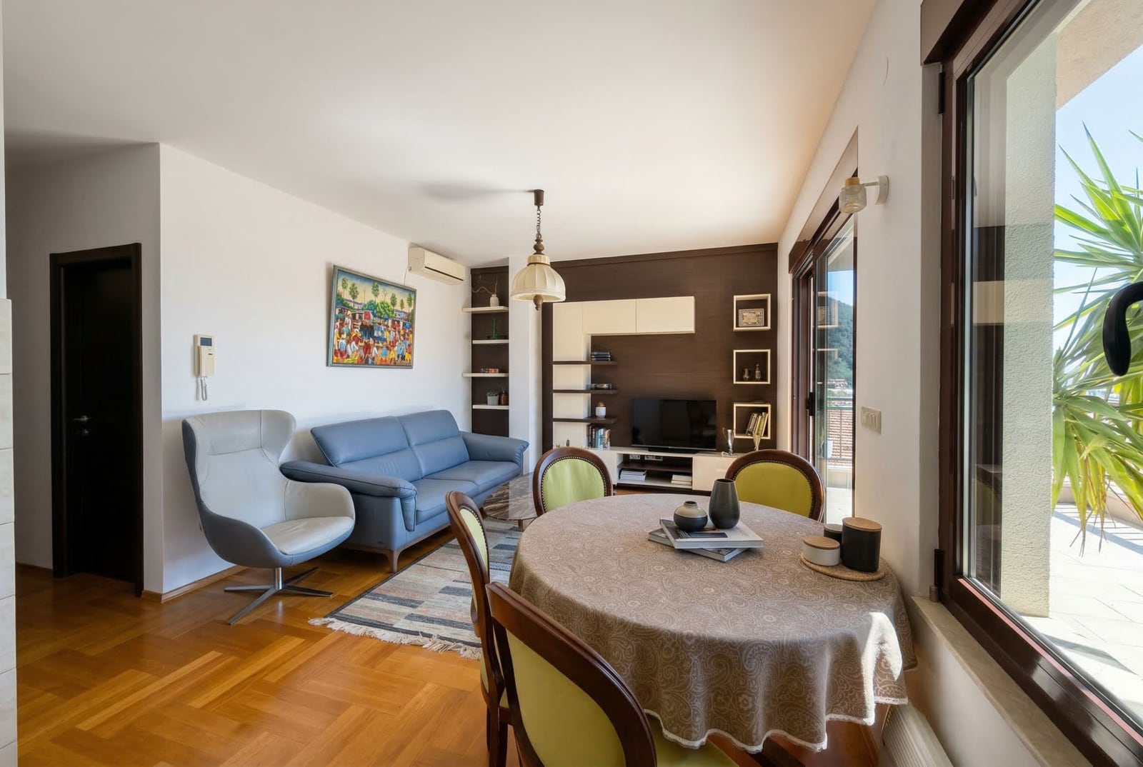 Living room with a blue sofa, dining area, and access to the terrace in an apartment in Budva, Montenegro.