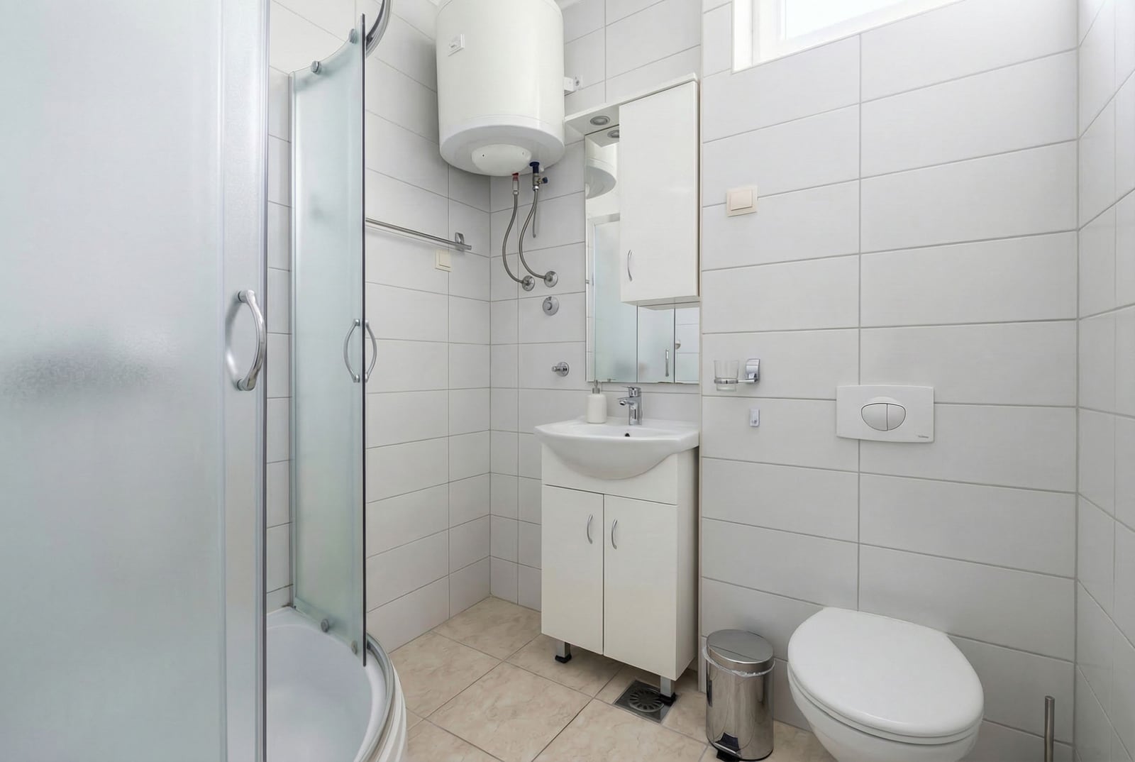 Bright bathroom in a studio in Budva, Montenegro: shower cabin, white fixtures, and a water heater on the wall.