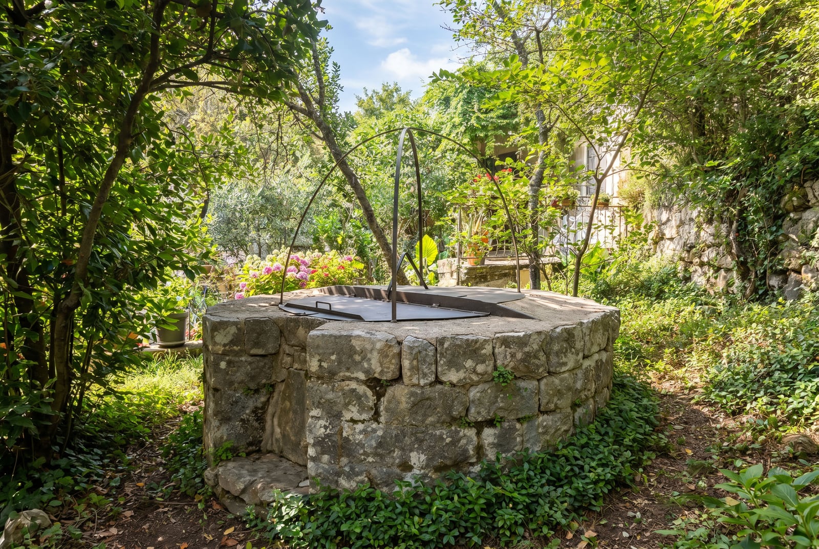 Antique stone well in a green garden on the grounds of a house in Dobrota, Montenegro. View of the property grounds.