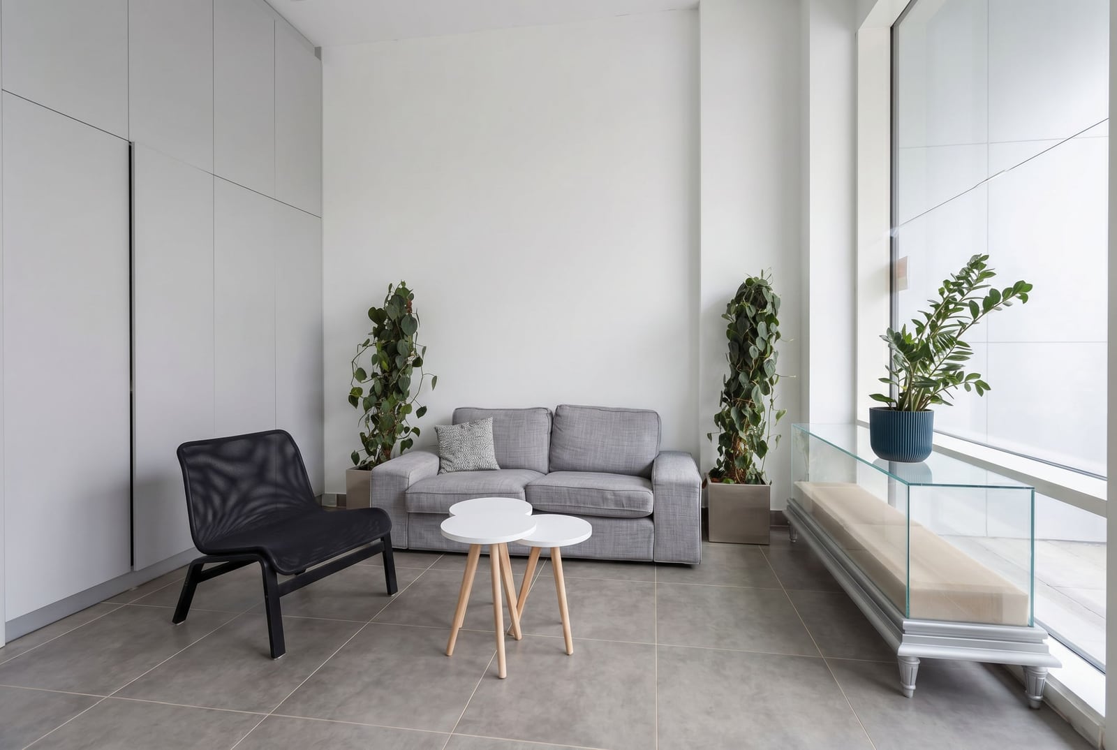 Modern living room in an apartment in Bečići, Montenegro: gray sofa, black armchair, panoramic windows, and plant decor.