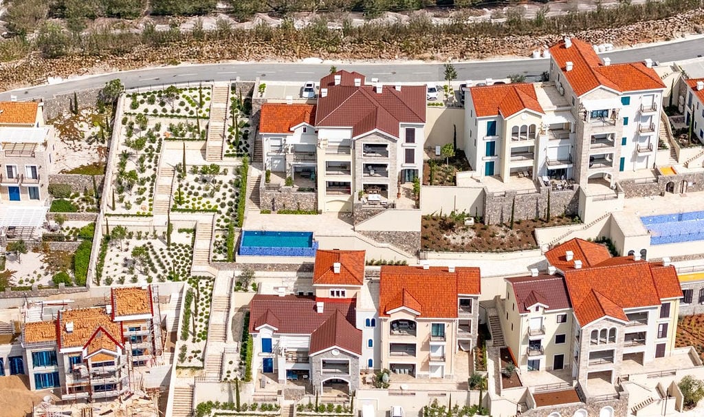 Aerial view of an elite residential complex in Luštica, Montenegro: villas with red roofs, terraces, and a swimming pool.