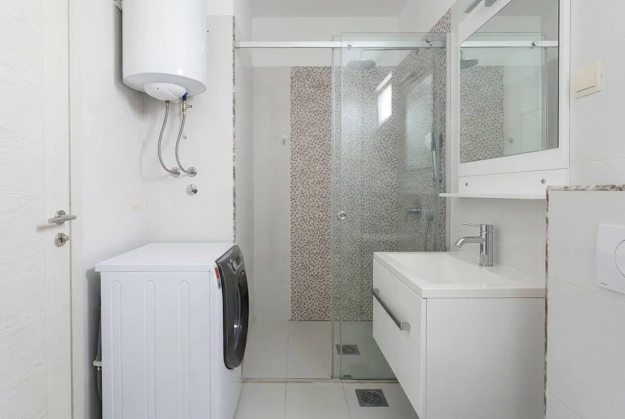 Bathroom featuring a glass shower, vanity sink, washing machine, and wall-mounted water heater.