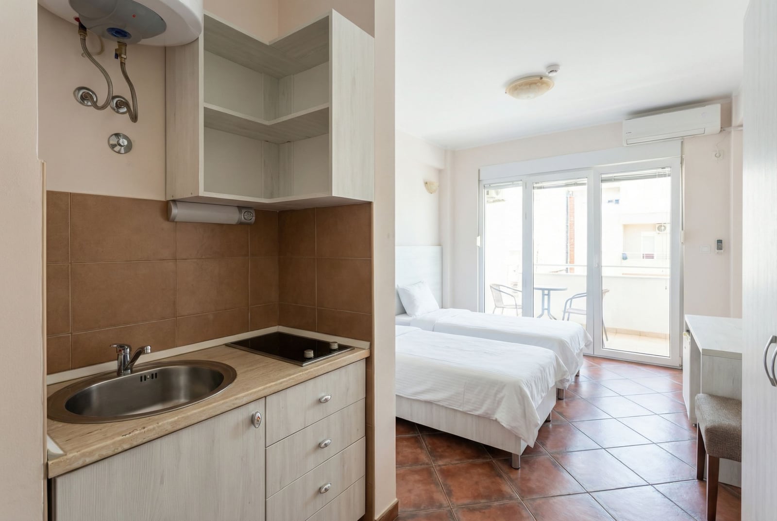 Studio kitchen with two beds and access to the balcony in a hotel, Bečići, Montenegro. Bright interior with tiled flooring.