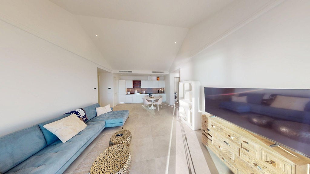 Modern living room with a blue sofa and kitchen in the Lustica Bay apartments, Montenegro. Bright interior with a TV area.