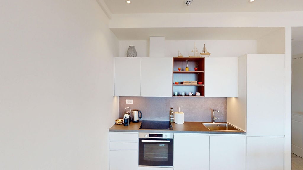 Modern white kitchen in an apartment in Luštica, Montenegro: built-in appliances, sink, and stylish open shelves.