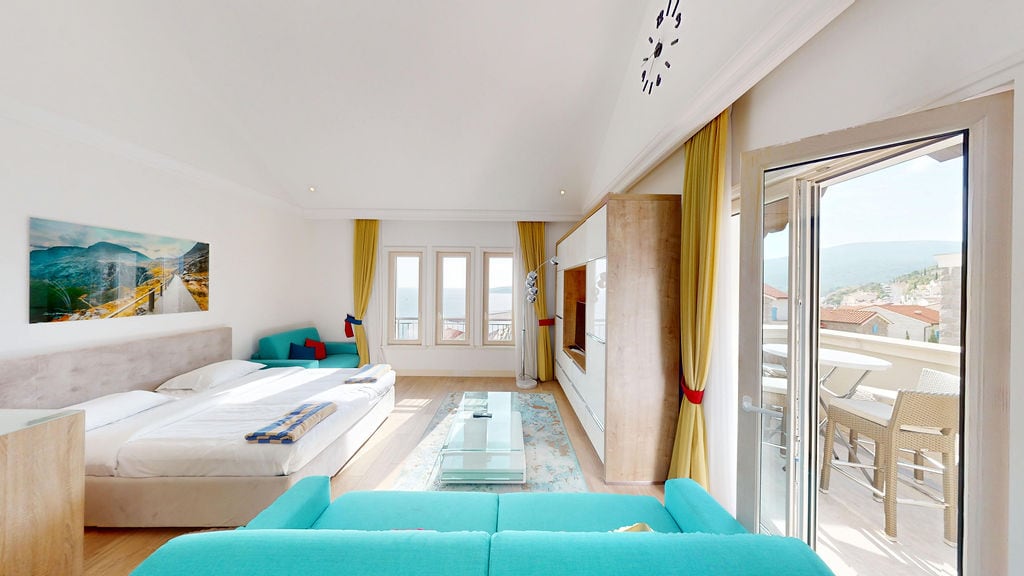 Bright bedroom with a double bed, turquoise sofa, and a terrace with a sea view in the Luštica residential complex, Montenegro.