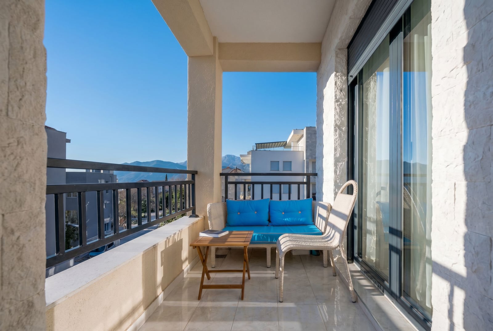 Cozy balcony with wicker furniture and mountain views in a Tivat apartment, Montenegro. Modern stone finish.