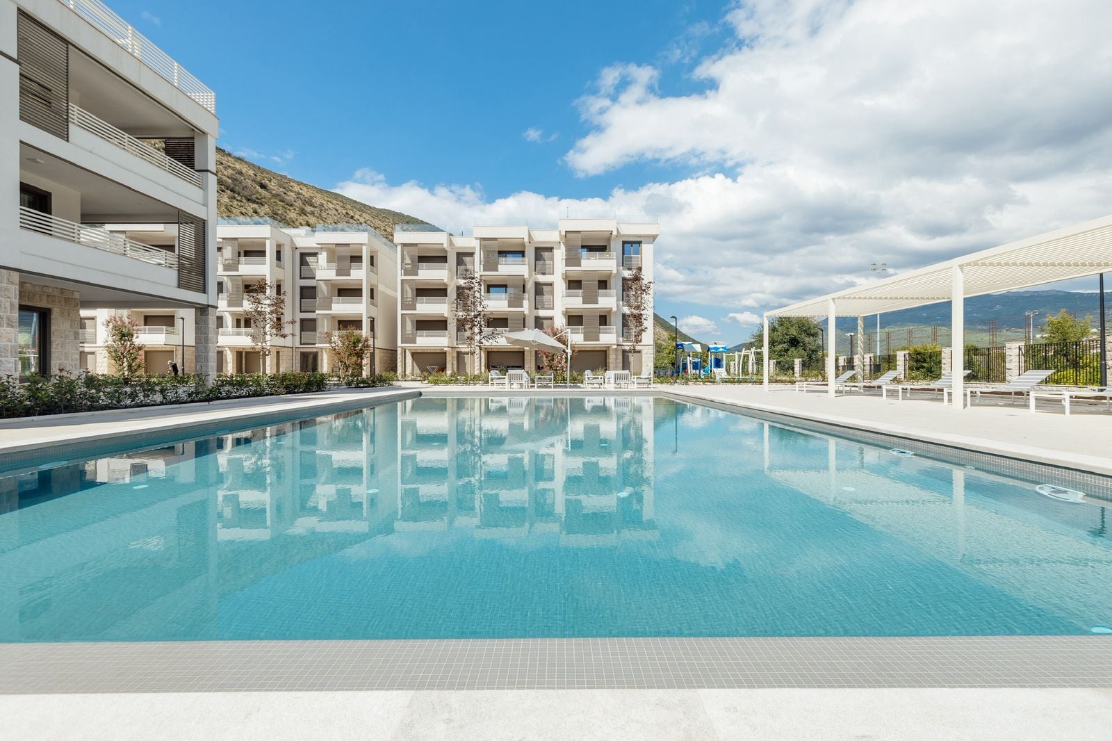 Outdoor pool at modern residential complexes in Igalo, Montenegro: a relaxation area with sun loungers and a mountain view.