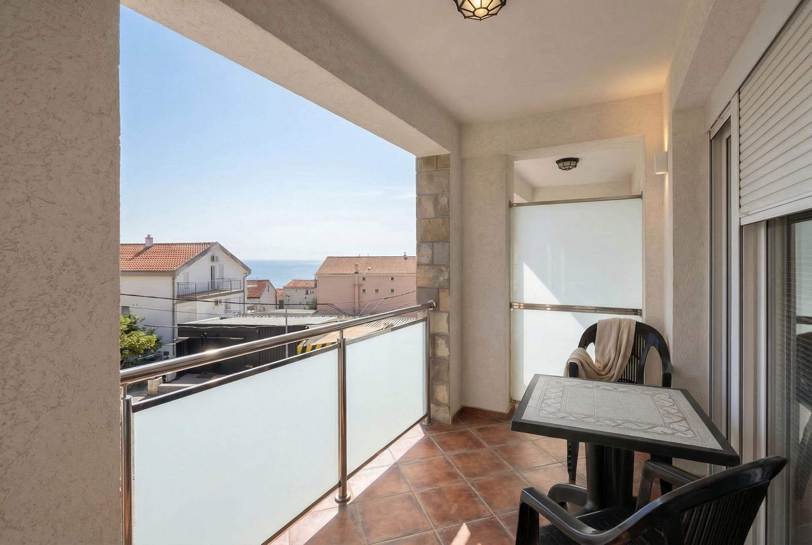 Balcony with sea view at a hotel in Bečići, Montenegro: tiled terrace with a table and chairs, glass railing.