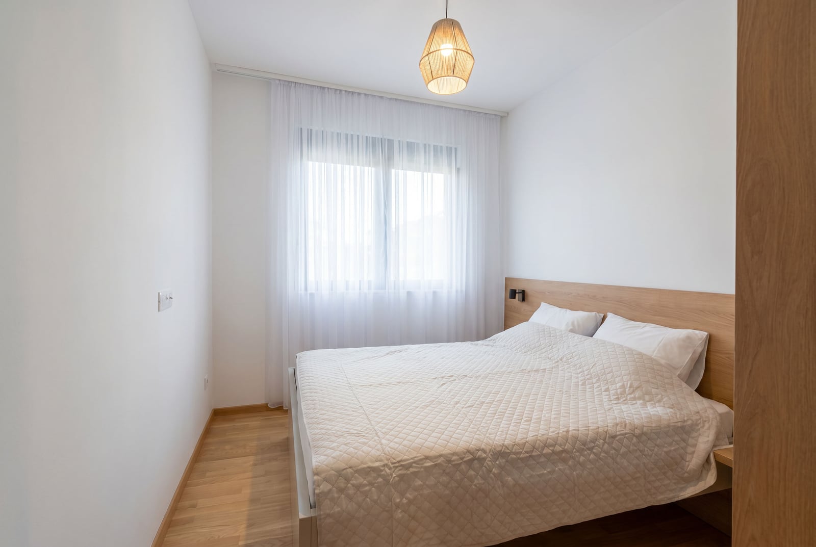 Bright bedroom with a double bed and a wooden headboard in a modern apartment, Budva, Montenegro.