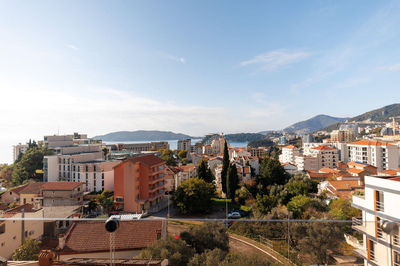 Panoramic view of the sea and the town of Becici, Montenegro, from a penthouse balcony featuring modern architecture and greenery.