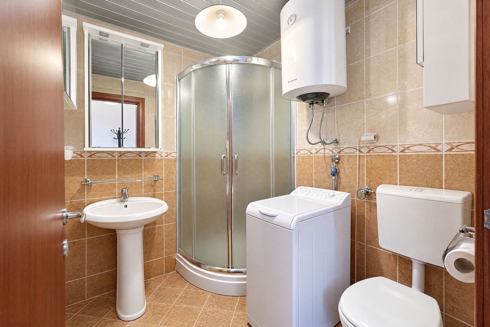 Bathroom featuring a shower stall, pedestal sink, toilet, and washing machine on beige tiles.
