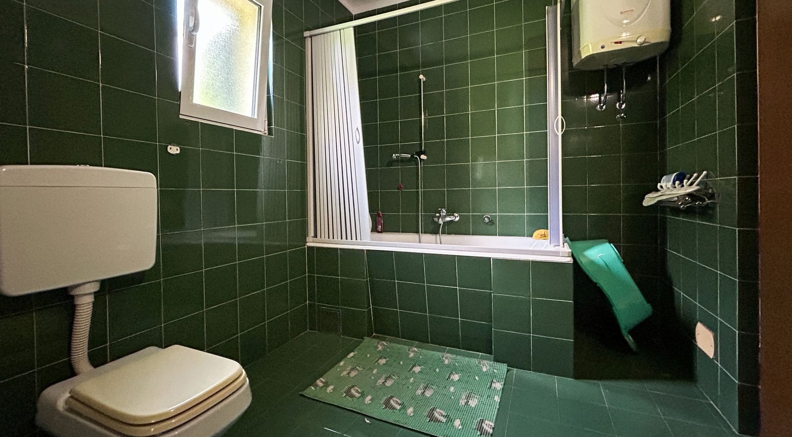 Bathroom with green tiles, a bathtub, and a boiler in a villa in Dobrota, Montenegro. Interior of the bathroom in the house.