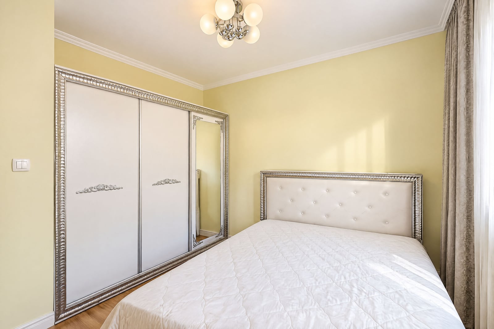 Bedroom featuring a white bed with an upholstered headboard and a large sliding wardrobe with a mirror.