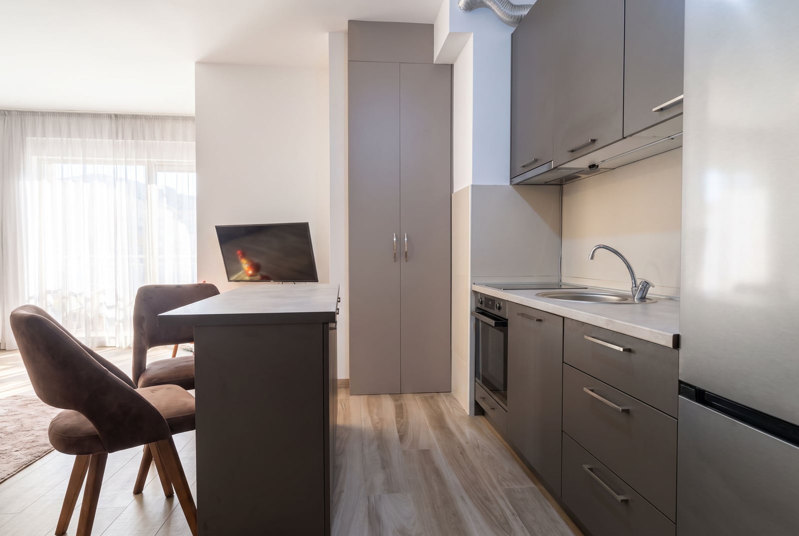 Modern kitchen with grey cabinets, an island, sink, oven, and refrigerator visible.