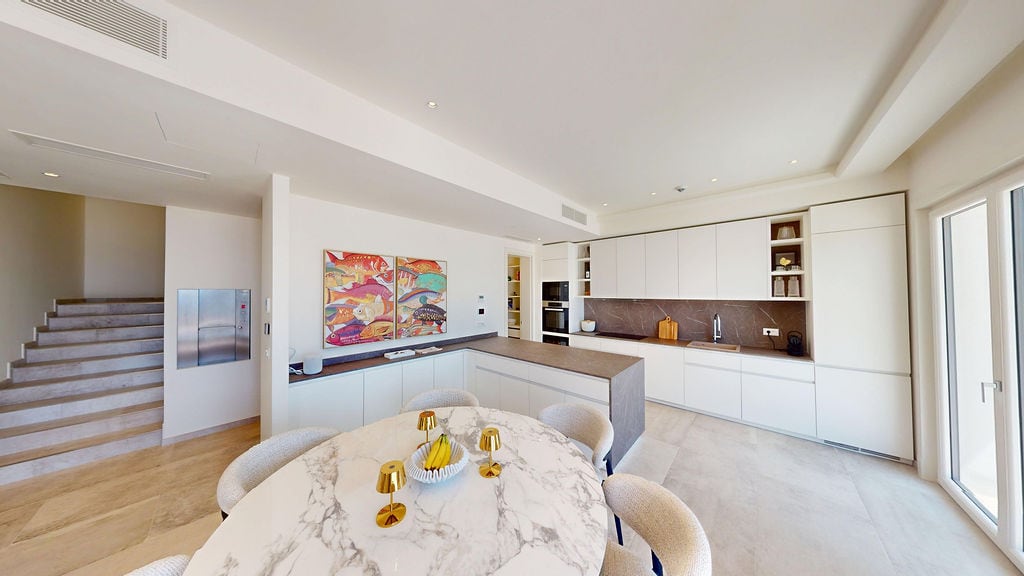 Modern kitchen-dining room with a marble table and white kitchen set in a villa in Luštica, Montenegro.