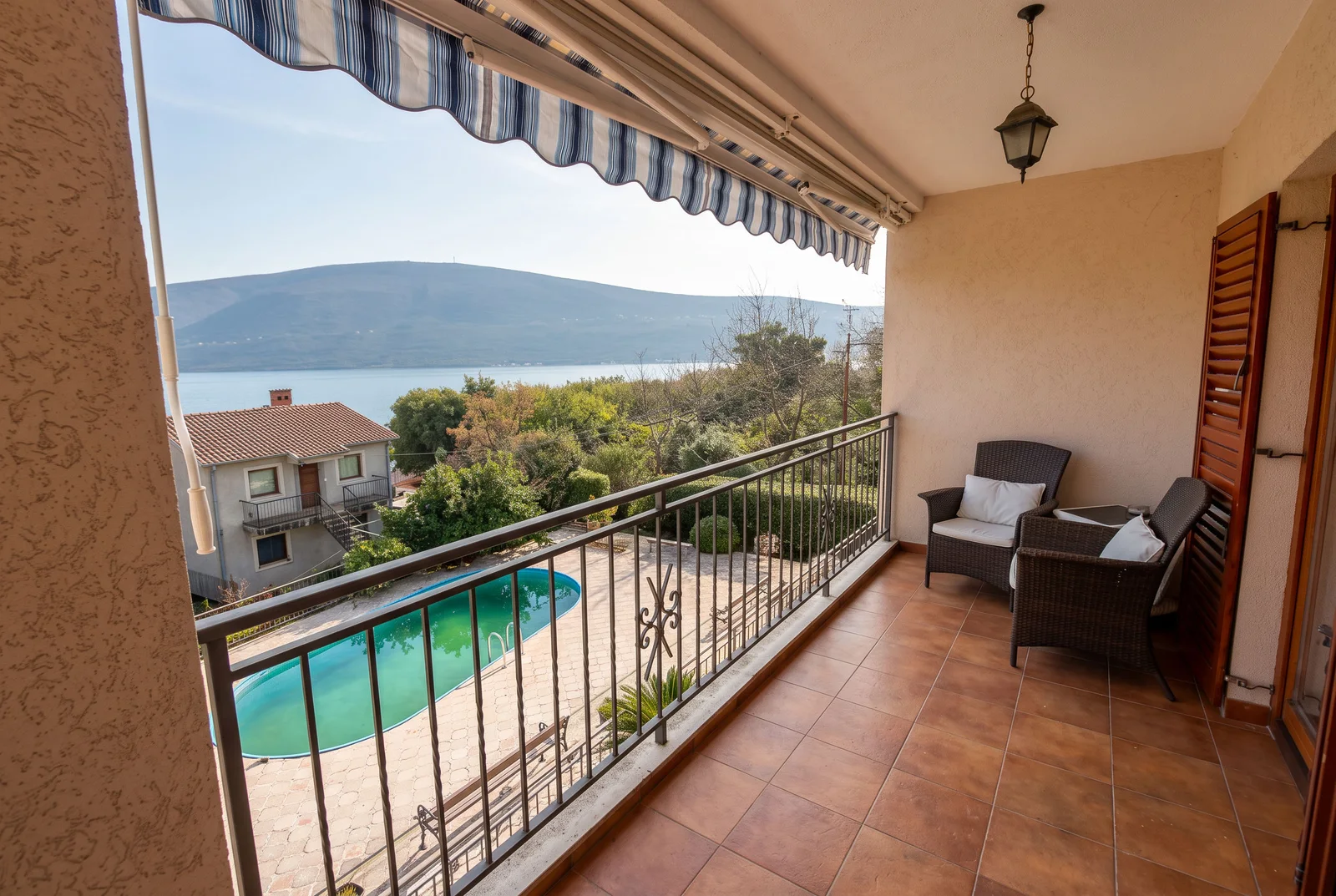 Balcony with wicker chairs and striped awning overlooking a pool and lake.