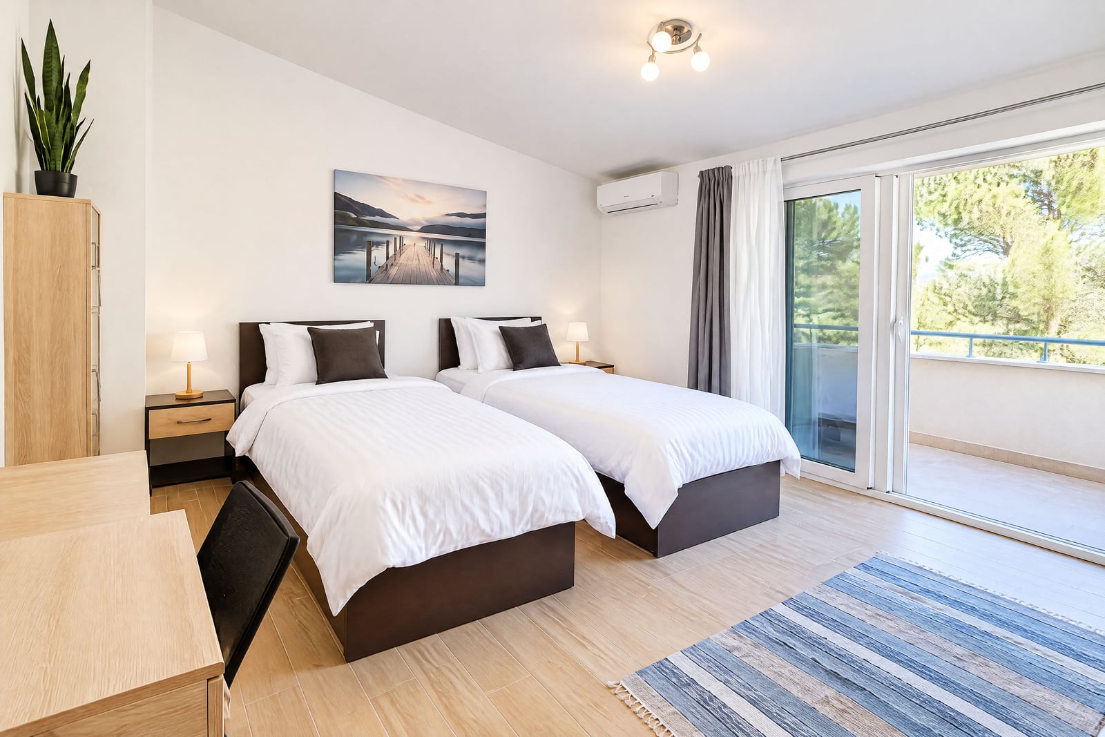 Modern bedroom with two single beds, wooden wardrobe, desk, and a sliding glass door leading to a balcony.