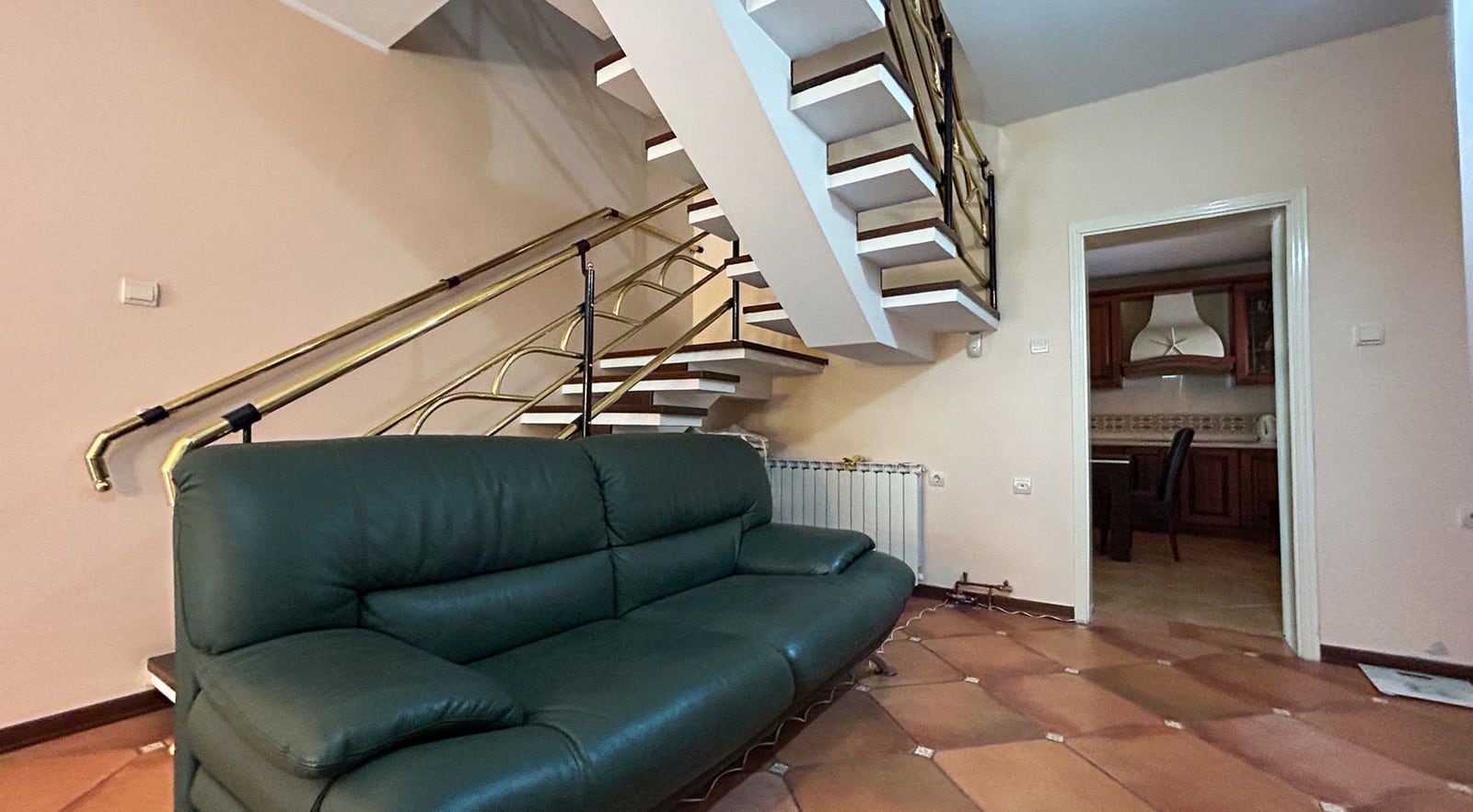 Living room with a leather sofa and staircase in a villa in Dobrota, Montenegro: interior with tile flooring and access to the kitchen.
