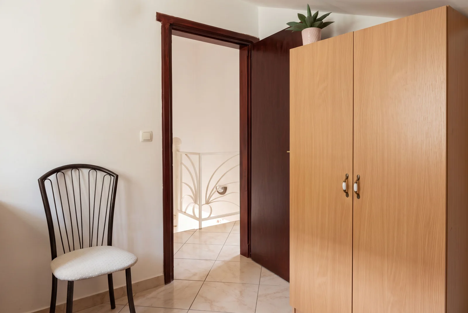 Hallway featuring a wooden wardrobe, metal chair, and an open door leading to a staircase landing.