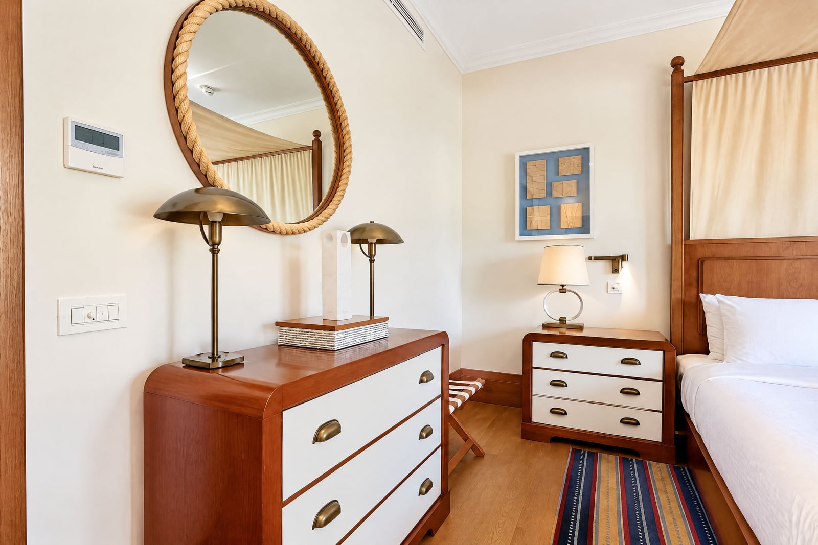 Bedroom featuring a wooden canopy bed, a dresser with a round rope-frame mirror, and brass lamps.