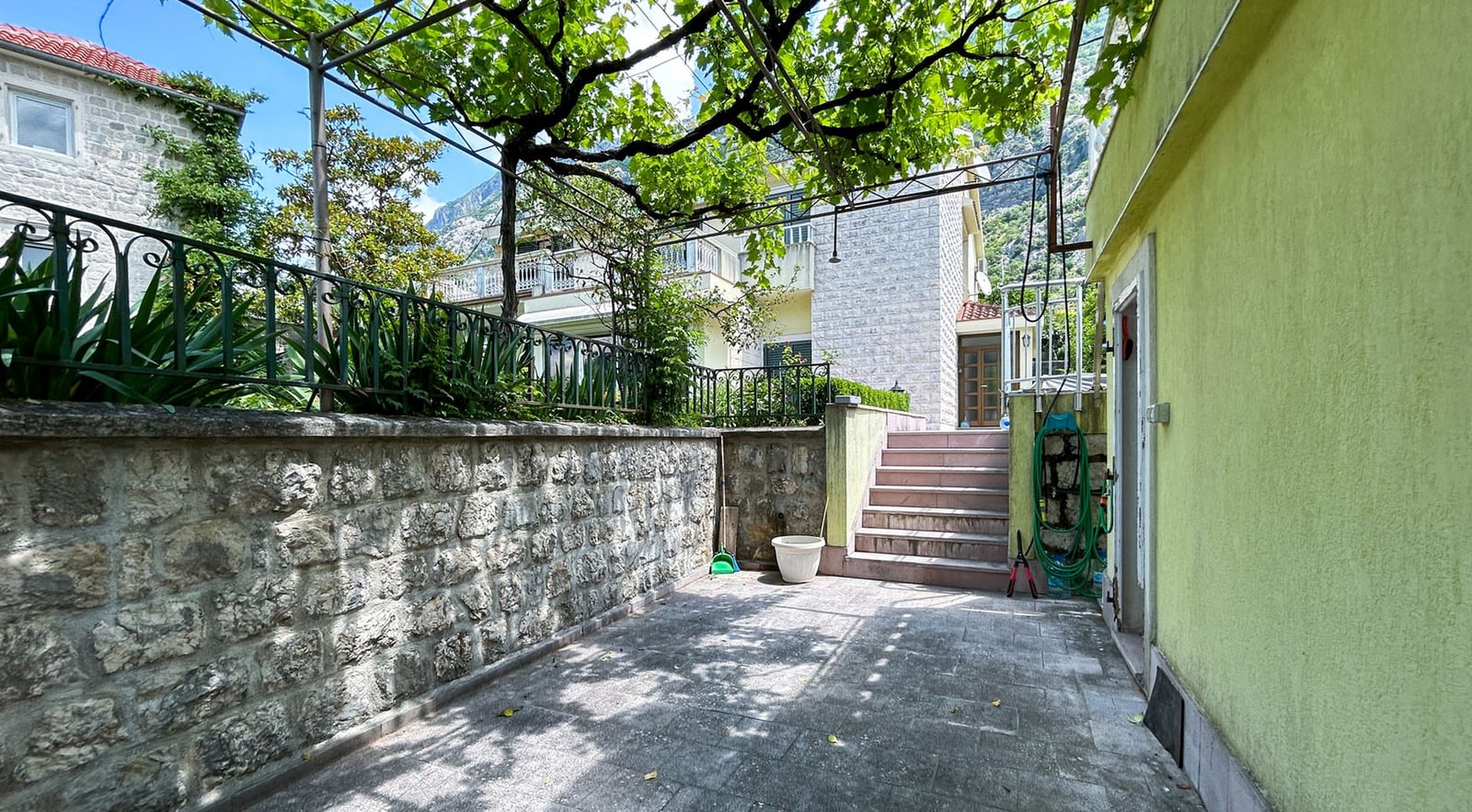 Cozy courtyard with a stone wall and grape pergola by a villa in Dobrota, Montenegro.
