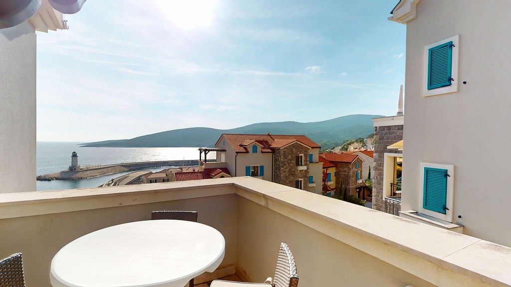 View from the balcony with furniture overlooking the sea, lighthouse, and mountains in the Luštica Bay residential complex, Montenegro.