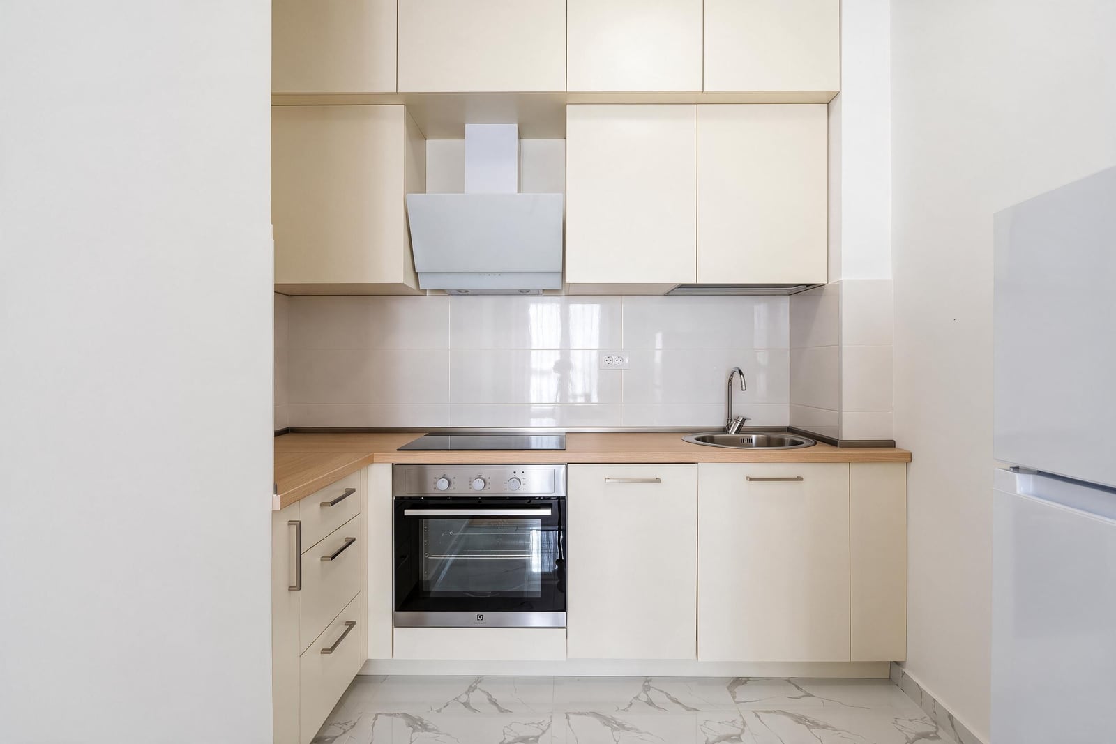 Modern kitchen with beige cabinets, built-in oven, cooktop, sink, and white range hood.