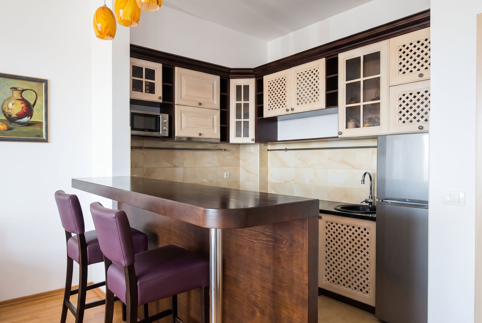 Cozy kitchen with wooden furniture, a bar counter, and purple chairs in an apartment in Bečići, Montenegro.
