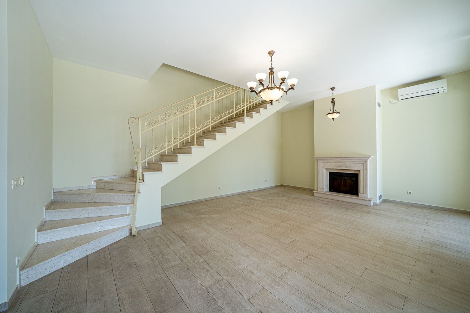Empty room featuring a staircase, fireplace, chandelier, light walls, and wood-look flooring.