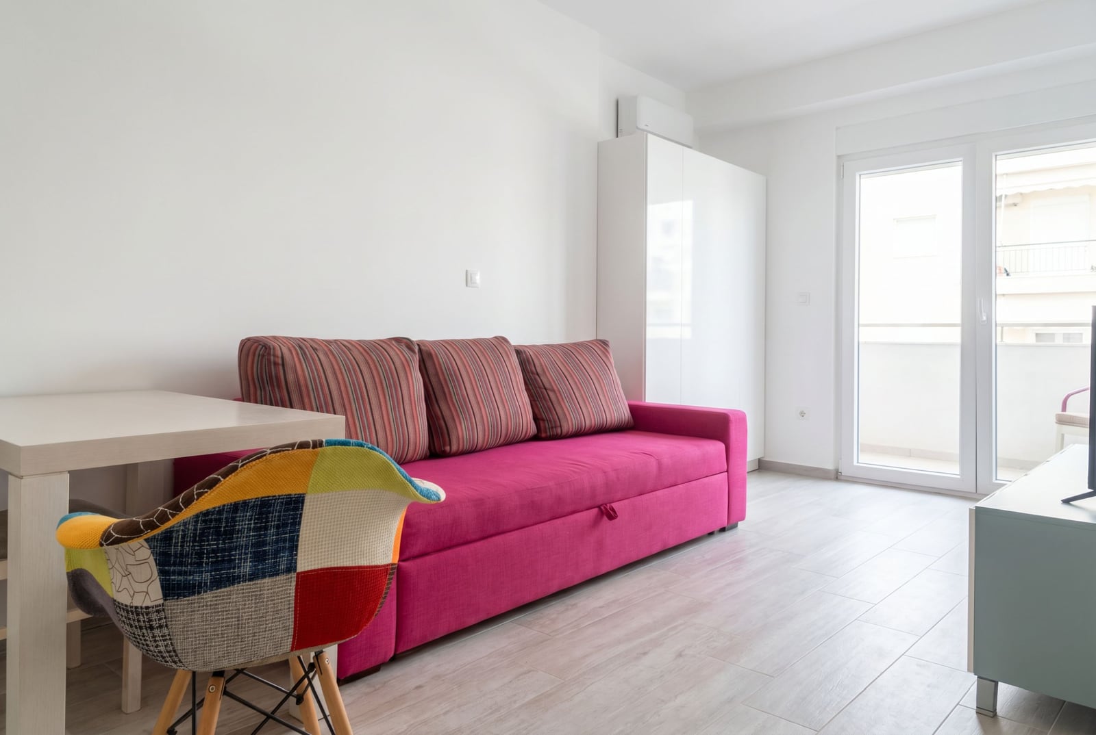 Living room in an apartment in Budva, Montenegro: a bright pink sofa, a designer chair, and access to the balcony.