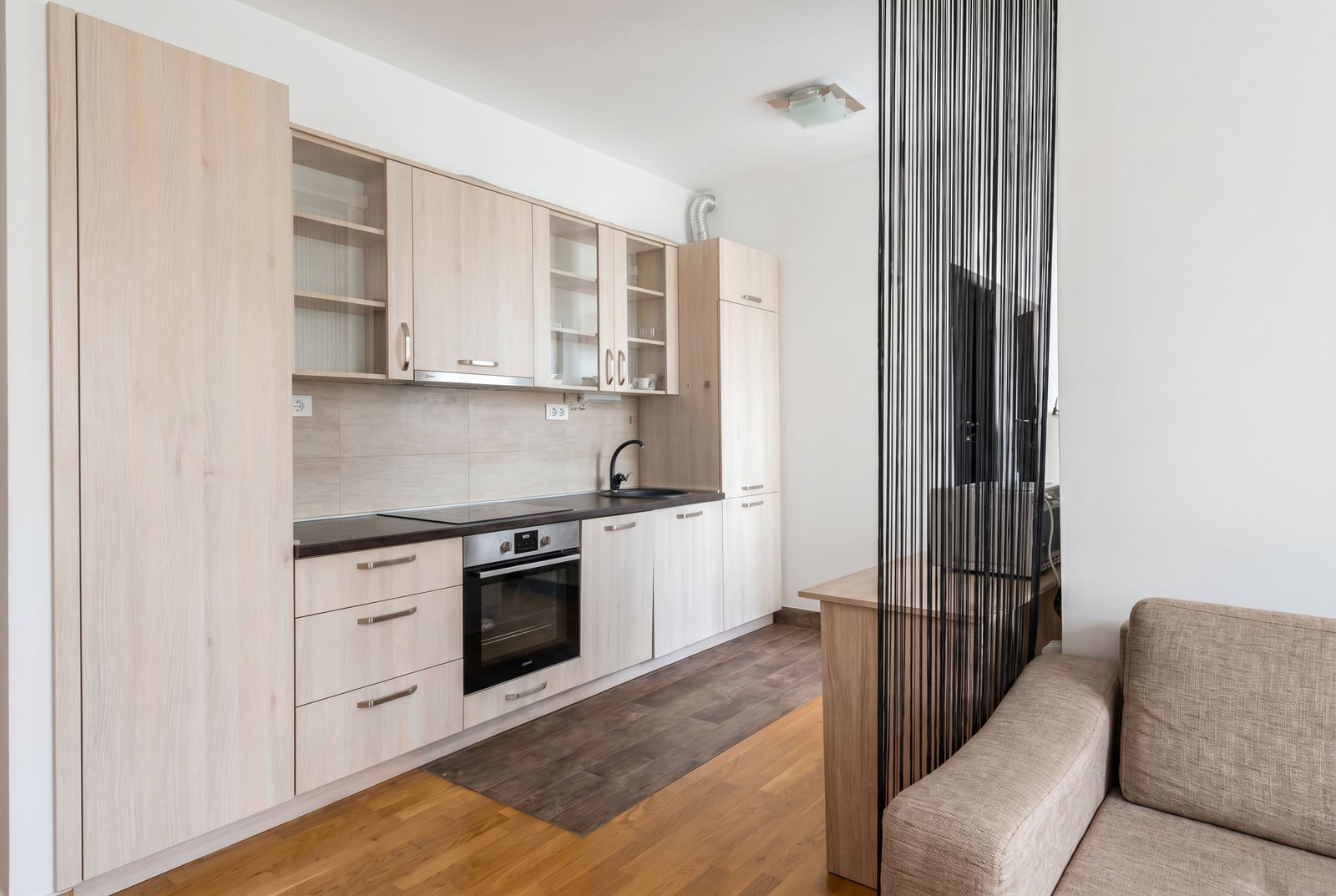 Modern bright kitchen in an apartment in Budva, Montenegro: built-in appliances, wooden facades, and a lounge area.
