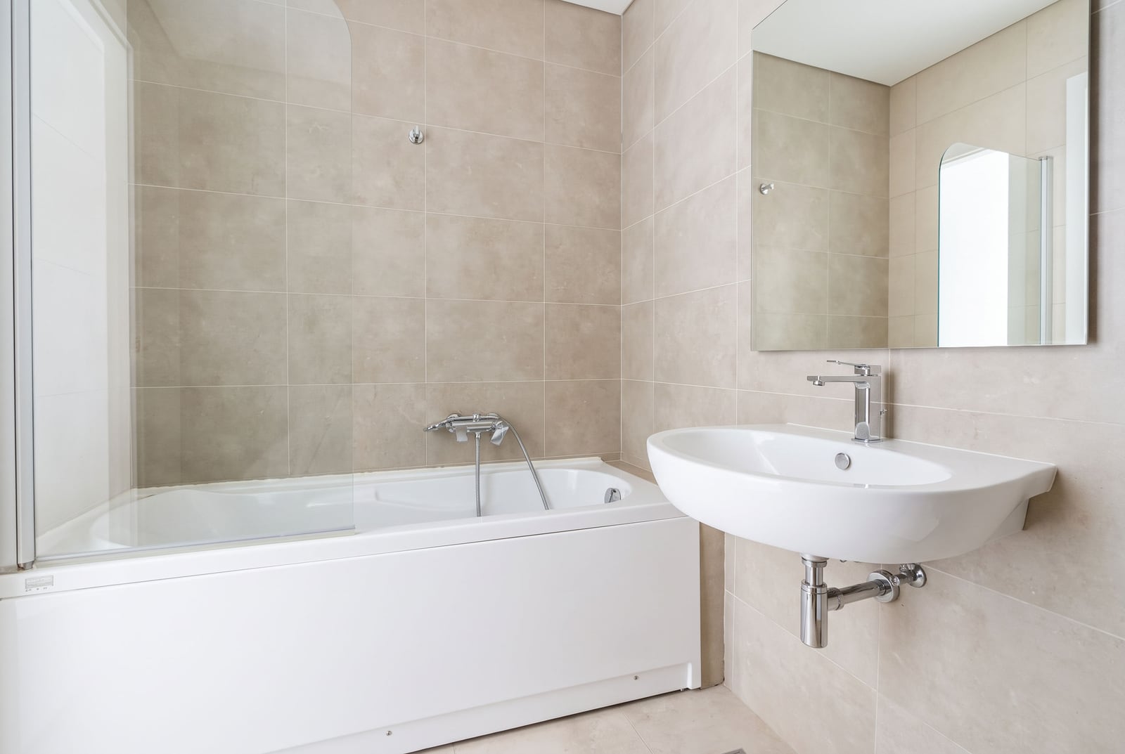 Bathroom featuring a white bathtub, wall-mounted sink, mirror, and beige tiled walls.