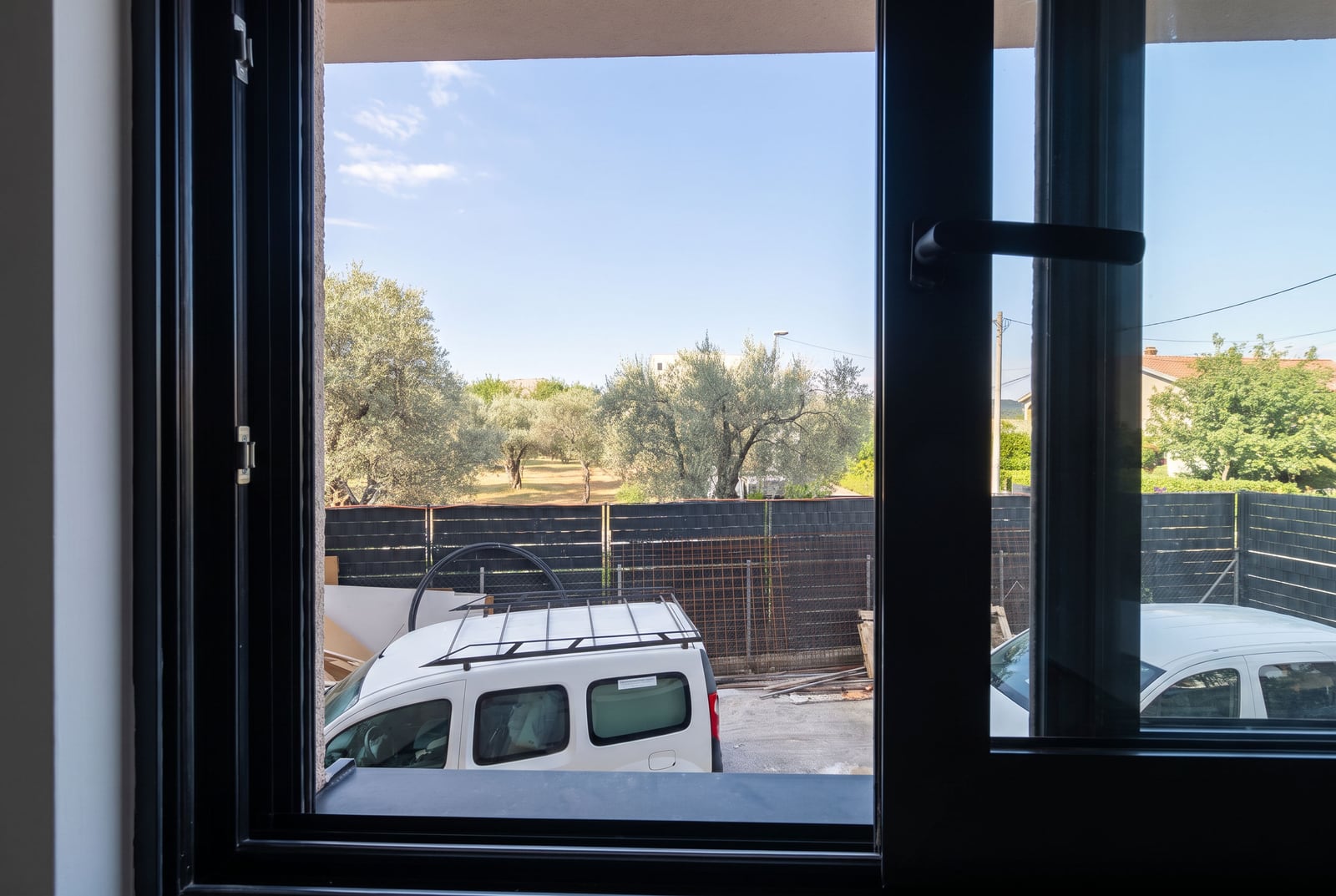 View from the plastic window of an apartment in Bar, Montenegro, overlooking the parking lot and olive garden.