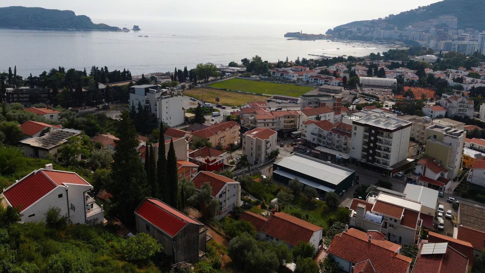 Panoramic view of Budva, Montenegro: land plot with a sea view, residential buildings, and the Adriatic coast.