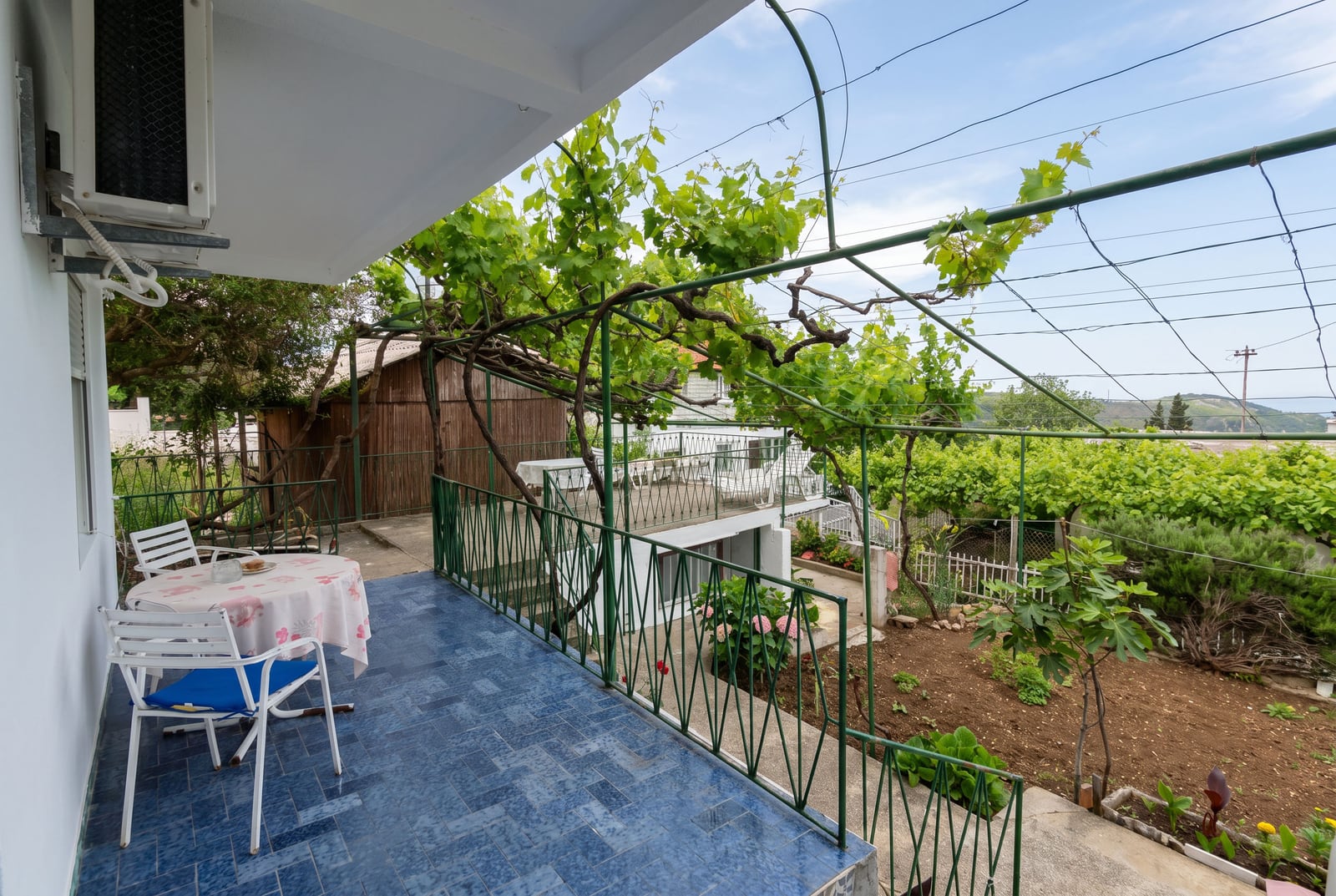 Cozy balcony with blue tiles and a dining area in a house in Sutomore, Montenegro, overlooking a green garden and a vineyard.