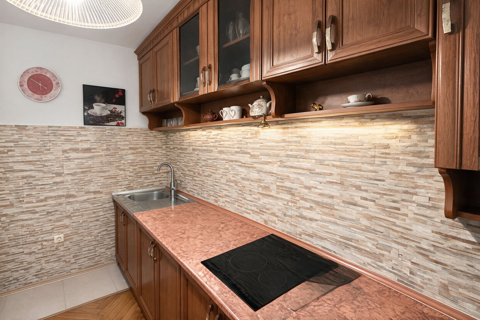Kitchen featuring wooden cabinets, a pink countertop, black induction cooktop, sink, and stacked stone backsplash.