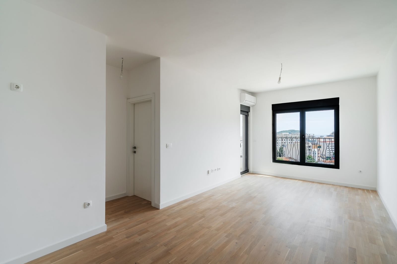 Bright empty living room with parquet flooring and a panoramic window in a new residential complex in Budva, Montenegro.