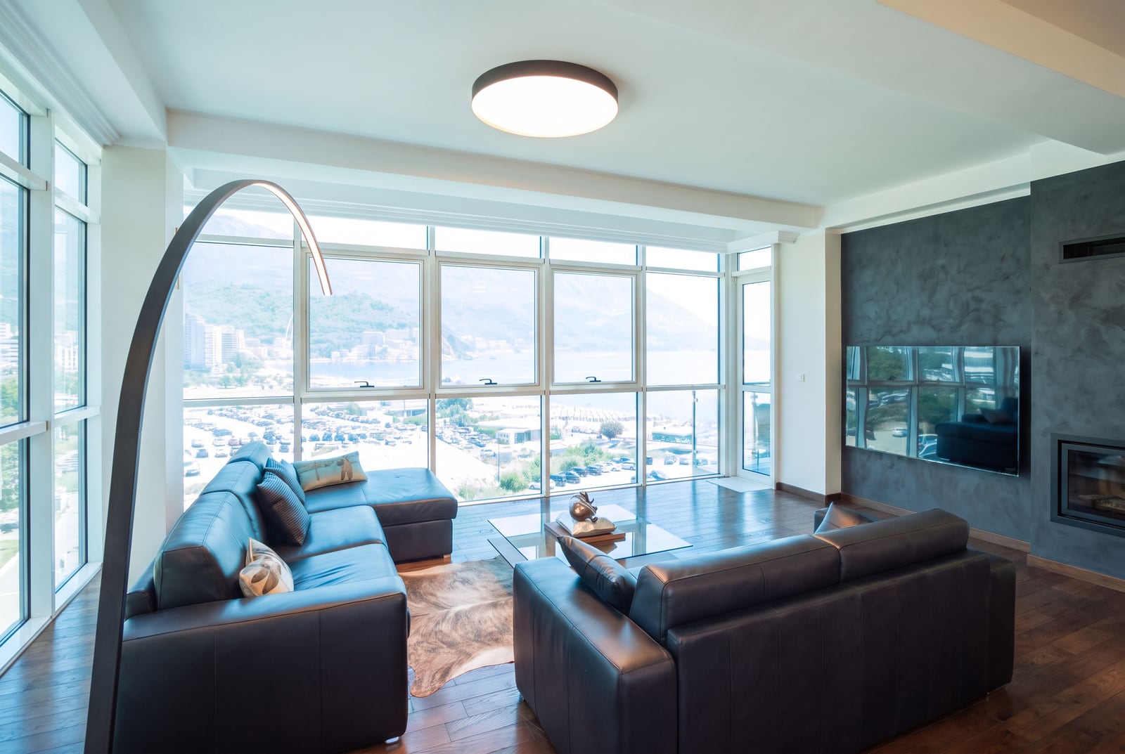 Bright living room with black leather sofas, a large arched floor lamp, and panoramic windows overlooking the water.