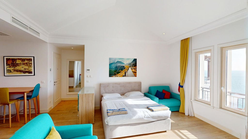 Bright bedroom in an apartment in Luštica, Montenegro: double bed, turquoise armchairs, and a sea view from the window.