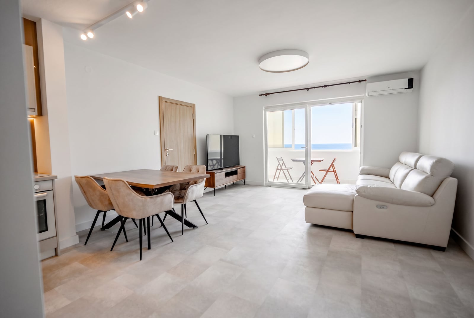Bright living room with a white sofa, dining area, and sea view in an apartment in Sveti Stefan, Montenegro.