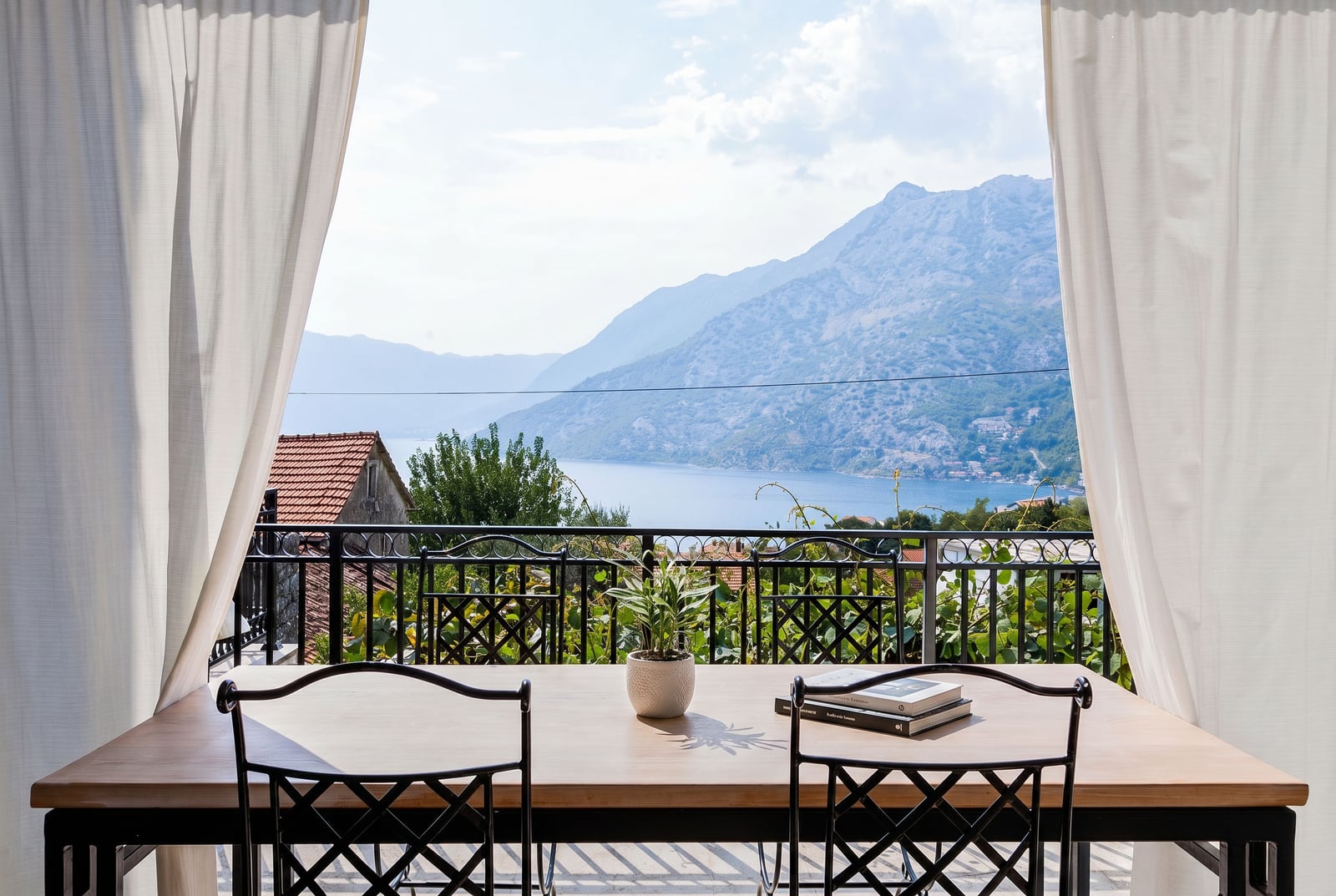 View from the balcony of an apartment in Risan, Montenegro: dining table, wrought iron chairs, and a panorama of the Bay of Kotor and the mountains.