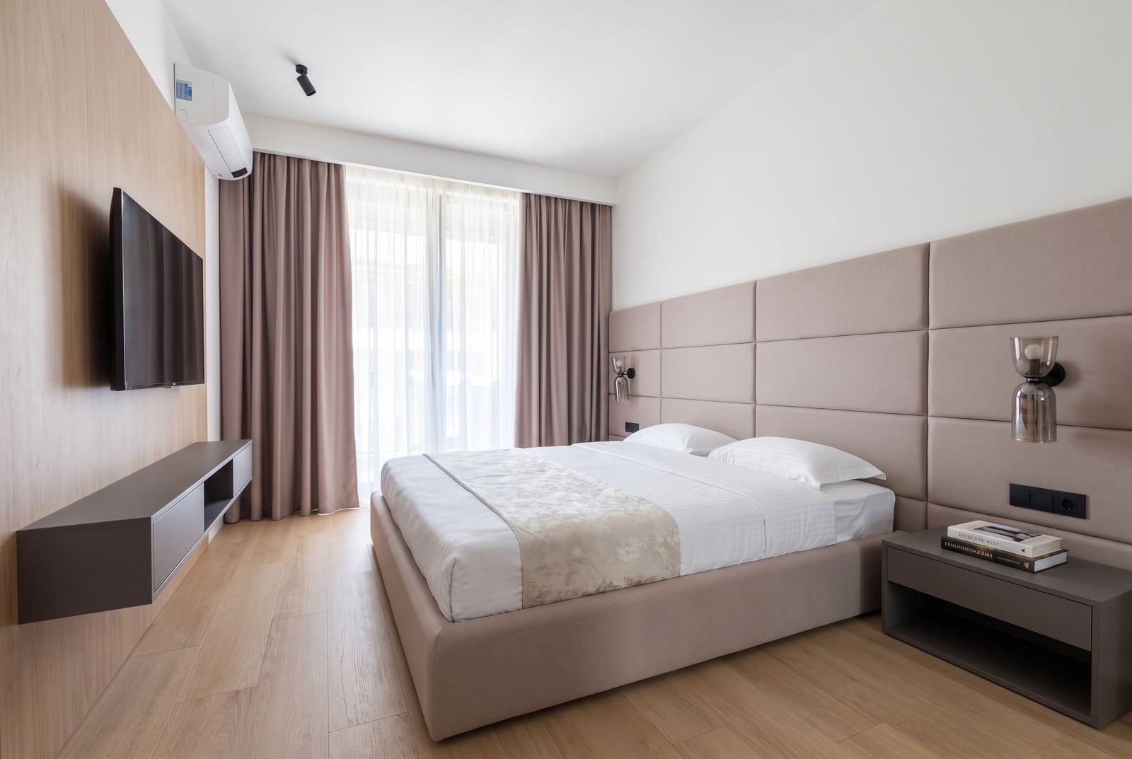 Modern bedroom with an upholstered bed headboard, TV area, and panoramic window in an apartment in Budva, Montenegro